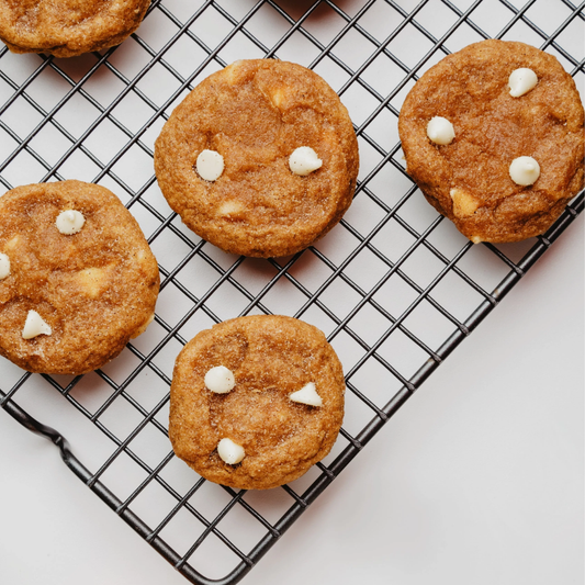 DIY Hunde Leckerlis mit weißen Drops auf einem Kuchengitter, selbstgemachte Hundekekse im herbstlichen Setting mit kleinem Zierkürbis auf hellem Hintergrund.